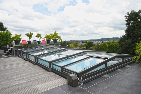 Eine flache, motorisierte Schwimmbadüberdachung mit Schiebetüren erweitert den Pool zum Minihallenbad, das auch an kühlen Tagen nutzbar ist. Die Überdachung verlängert die Badesaison und schützt vor Verunreinigungen und Unfällen.