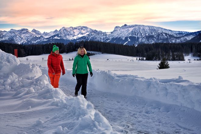 Der zugefrorenen Attlesee liegt unter einer dicken Schneedecke, am Horizont ragen die Allgäuer und Tiroler Gipfel auf.